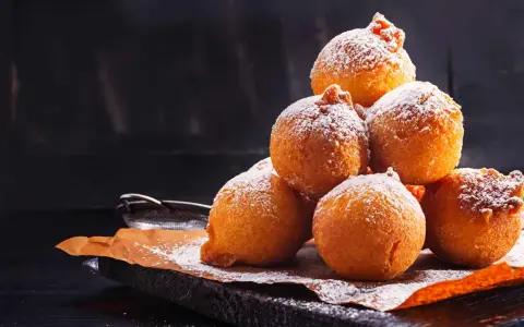 Pile di frittelle di mele e uvetta con lievito di birra, spolverate di zucchero a velo, su carta da forno.