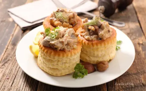 Tre vol-au-vent con funghi cremosi, guarniti con prezzemolo e aneto, su un piatto bianco con spicchi di limone.