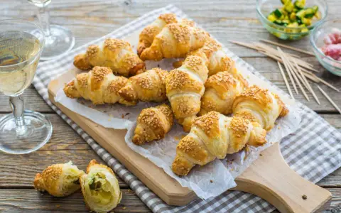 Croissant dorati con ripieno di pasta sfoglia e semi di sesamo, pronti per essere gustati con un bicchiere di vino.