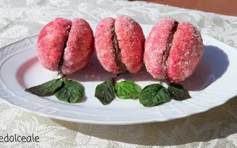 Tre dolci pesche abruzzesi ricoperte di zucchero, con un ripieno scuro, adagiate su un piatto bianco con foglie verdi.