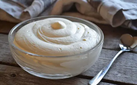Una ciotola di soffice crema al mascarpone senza lattosio, pronta per essere gustata. Un cucchiaino argentato attende accanto.