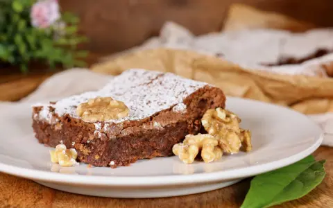 Una fetta di torta noci e cioccolato senza farina, cosparsa di zucchero a velo e decorata con noci intere.