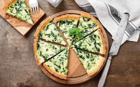 Torta salata spinaci e mozzarella, con un tocco di speck affumicato, tagliata a spicchi su un tagliere di legno.