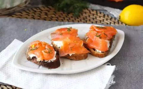 Tre bruschette con salmone affumicato, formaggio cremoso e aneto, guarnite con scorza di limone.
