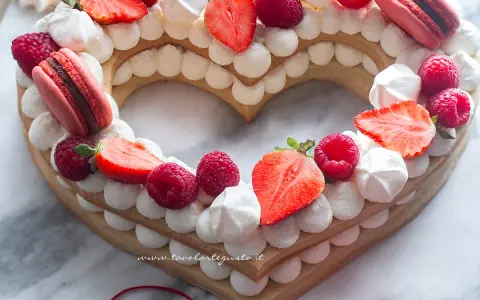 Cream tart numero 1 a forma di cuore, decorata con panna, fragole, lamponi e macarons.