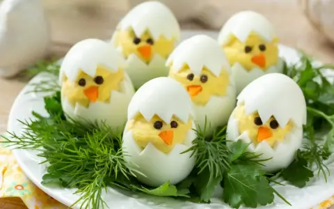 Uova sode ripiene a forma di pulcino, un'idea divertente per le jajka faszerowane pasquali, adagiate su un letto di erbe aromatiche.