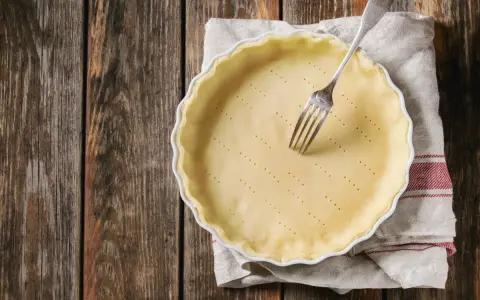 Pasta frolla salata con olio e parmigiano pronta per essere infornata. Una forchetta è appoggiata sulla base bucherellata.
