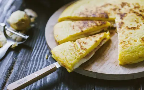Focaccia di patate in padella con prosciutto cotto e formaggio, tagliata a spicchi su un tagliere di legno.