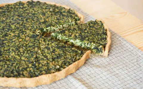 Una fetta di torta salata vegana spinaci, con una crosta dorata e un ripieno verde e cremoso, pronta per essere gustata.