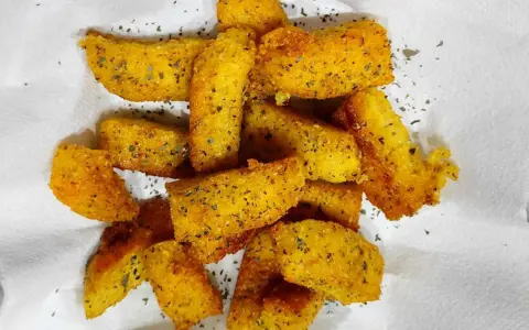 Croccanti bastoncini di polenta taragna fritta, dorati e conditi con erbe aromatiche, adagiati su carta bianca.