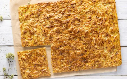 Schiacciata di zucchine e cipolle dorata e croccante, tagliata a pezzi su carta da forno.