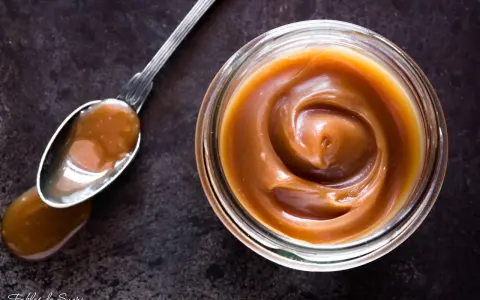 Un cucchiaio pieno di crema pasticcera al caramello salato, accanto a un barattolo dello stesso delizioso composto.