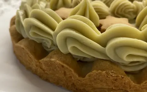 Torta con bordi croccanti e un abbondante strato di ganache pistacchio, decorata con biscotti a forma di stella.