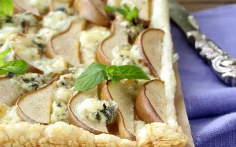Deliziosa pizza zola e pere su pasta sfoglia croccante, guarnita con foglie di menta fresca. Un connubio di sapori unico.