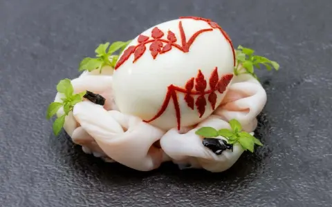 Uovo sodo decorato con motivi rossi, adagiato su un letto di calamari crudi e guarnito con erbe aromatiche. Un barzotto uovo elegante.
