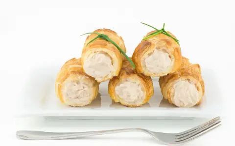 Cannoli salati ripieni di tonno, guarniti con erba cipollina, su un piatto bianco con forchetta.