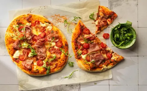 Pizza con mascarpone, pomodorini, prosciutto crudo e rucola, su carta forno.