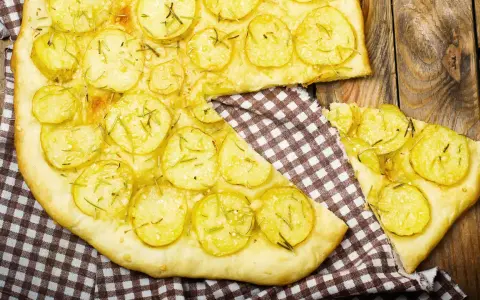 Schiacciata di patate con farina di ceci, guarnita con rosmarino fresco, su un tagliere di legno rustico.