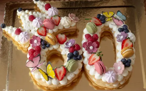 Una torta numero 60 decorata con panna, frutta fresca, macarons e farfalle. Una deliziosa ricetta torta numero per festeggiare.