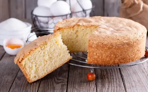 Un soffice ciasto drozdzowe, appena sfornato, con una fetta tagliata. Ingredienti per la torta lievitata sono visibili sullo sfondo.