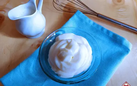 Crema soffice e vellutata, una delizia preparata con yogurt greco. Accanto, una piccola brocca e una frusta, pronti per creare altre bontà.