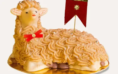 A decorative cake shaped like a lamb, with piped frosting and a red ribbon.