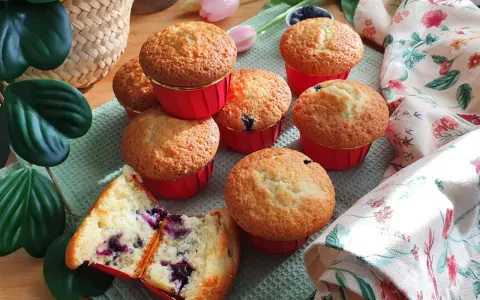 Morbidi muffin ai mirtilli, uno tagliato a metà rivela il suo interno succoso. Perfetti per una colazione o merenda golosa.