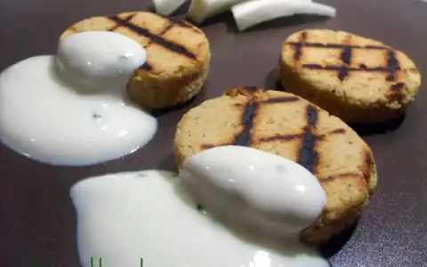 Deliziosi medaglioni di ceci grigliati, serviti con una salsa bianca cremosa e guarniti con erbe aromatiche.