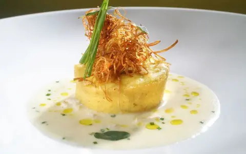Flan di porri con salsa di acciughe, guarnito con cipolla croccante e erbe aromatiche. Un piatto raffinato che celebra i sapori del mare e della terra.