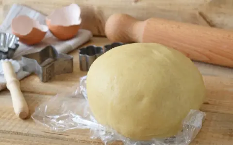 Impasto per kruche ciasto, stampini per biscotti, gusci d'uovo e mattarello pronti per preparare dolci deliziosi.