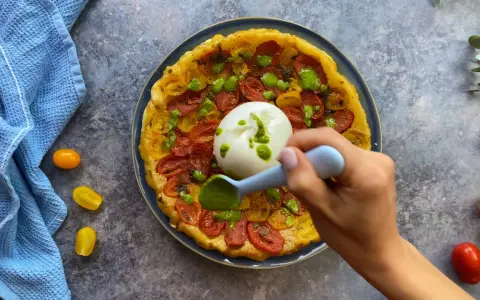 Tarte tatin pomodorini e burrata, con una mano che aggiunge un pesto verde.
