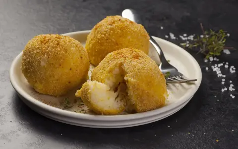 Tre arancini dorati su un piatto, uno aperto rivela il ripieno di riso. Un invito a provare il nostro arancini ricetta.
