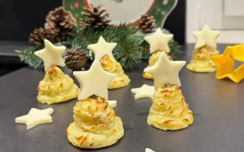 Alberelli di patate decorati con stelle di formaggio, su un piatto natalizio con pigne e rami di abete.