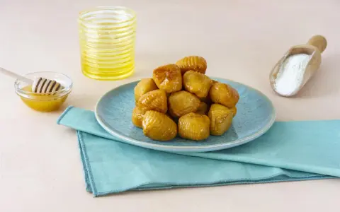 Un mucchio di turdiddri calabresi lucidi di miele su un piatto blu, con miele e farina a lato.