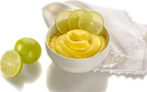 Una ciotola di cremosa crema al lime, guarnita con fette di lime fresco e accompagnata da lime interi e a metà.