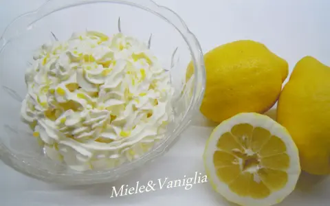 Una ciotola di panna montata con scorza di limone, accanto a limoni freschi. Perfetta per una ganache al limone leggera e profumata.