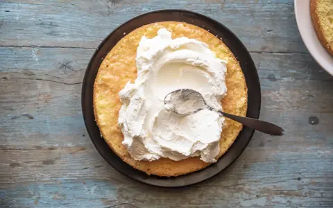 Una fetta di pan di spagna attende la sua deliziosa crema allo yogurt, spalmata con un cucchiaino.