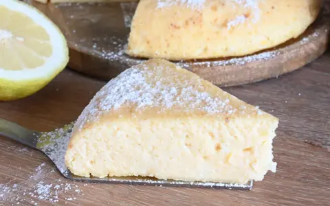 Una fetta di torta con semola, spolverata di zucchero a velo, accanto a un limone fresco.