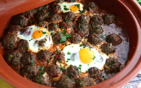 Polpette marocchine in umido con uova cotte nel tajine, guarnite con prezzemolo fresco.