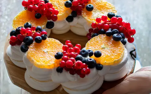 Delizioso tort pavlova a forma di corona, decorato con fette d'arancia, ribes rosso e mirtilli.