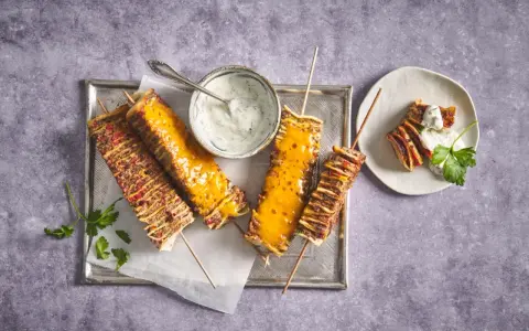Tortilla kebab su spiedini, alcuni ricoperti di formaggio fuso, serviti con salsa allo yogurt e prezzemolo.