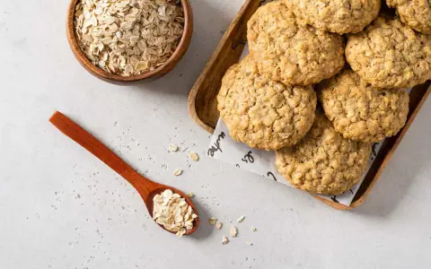 Biscotti di avena dorati e croccanti, con fiocchi d'avena in una ciotola e un cucchiaio.