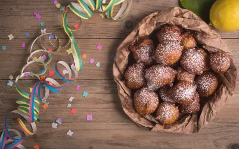 Castagnole abruzzesi cosparse di zucchero a velo, pronte per Carnevale, con coriandoli e stelle filanti su tavola di legno.
