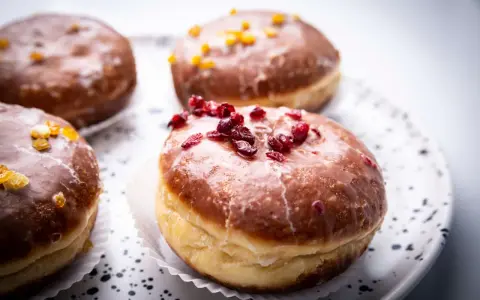 Paczki ricchi e golosi, con glassa lucida e decorazioni di frutta secca. Un invito a provare il paczki przepis perfetto.