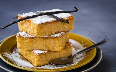 Tre fette impilate di torta di riso fiorentina, spolverate di zucchero a velo e decorate con baccelli di vaniglia.