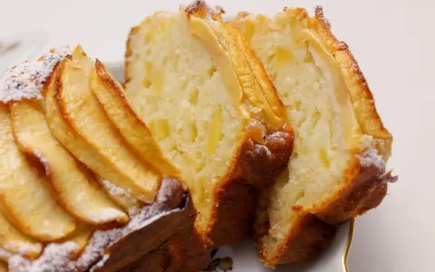 Fette di plumcake ricotta e mele, con mele a vista sulla superficie e spolverata di zucchero a velo.