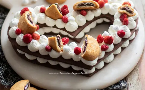 Cuore di pasta biscotto al cacao per cream tart, decorato con panna, fragoline e biscotti ripieni.