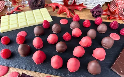 Cioccolatini al lampone, alcuni ricoperti di cioccolato fondente, altri di rosa, con lamponi freschi e tavoletta di cioccolato bianco.