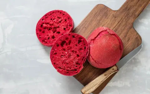 Pane alla barbabietola, un panino rosso vibrante tagliato a metà su un tagliere di legno, pronto per essere gustato.