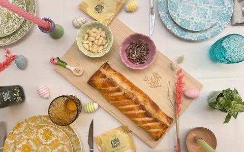 Torta pasqualina senza uova dorata, con mandorle e pinoli, decorata con uova colorate e candela pasquale.
